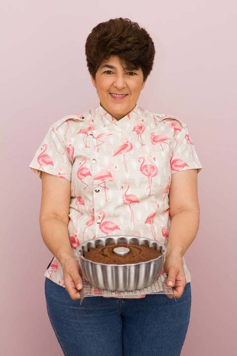 Confeiteira vestida com dolmã segura um bolo caseiro de chocolate ainda na assadeira'