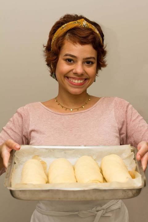 Laura Ferraz da pãezinhos da Laura segurando uma assadeira com vários pães de batata prontos para irem ao forno'