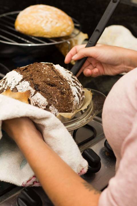 pão de fermentação natural sendo retirado da assadeira com a ajuda de um pano e uma espátula'