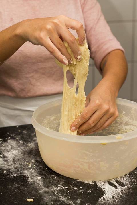massa de pão de batata sendo sovada por duas mãos femininas em uma cozinha'