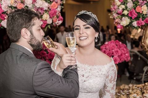 Primeira brinde dos noivos Maria Eduarda e Gabriel na festa de casamento sob luzes quentes e dinâmicas'