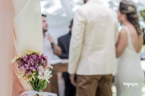Detalhe da flor com noivos ao fundo em desfoque. Foto registrada pelo fotográfo de casamentos em BH Rapha Drummond.'