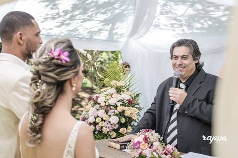 Fotografia do Pastor em orátoria e do Casal juntos e de costas, sobre a tenda onde ocorria a cerimônia de casamento, momento registrado pelo fotógrafo de casamentos em BH Rapha Drummond. '