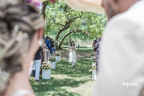 Fotógrafo de casamentos em BH Rapha Drummond registra momento em que as alianças estão chegando com a daminha em foco pela nave do local onde está sendo realizado o casamento.'