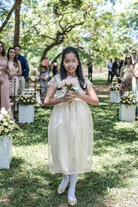 Fotográfo de casamentos tira foto em close da daminha com buque em mãos trazendo as alianças aos noivos.'
