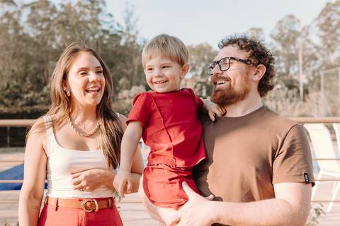 Família sorrindo no gramado externo da festa, com decoração ao fundo'