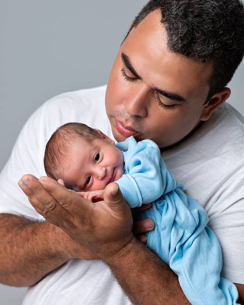 Ensaio Newborn Natal/RN. Foto de recém-nascido sendo segurado pelo pai.'