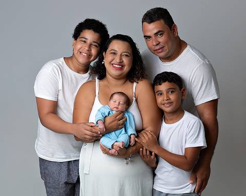 Ensaio Newborn em Natal/RN no Estúdio Amoradia Foto. Foto de recém-nascido sendo segurado pela mãe, ao lado estão o pai e os dois irmãos mais velhos.'