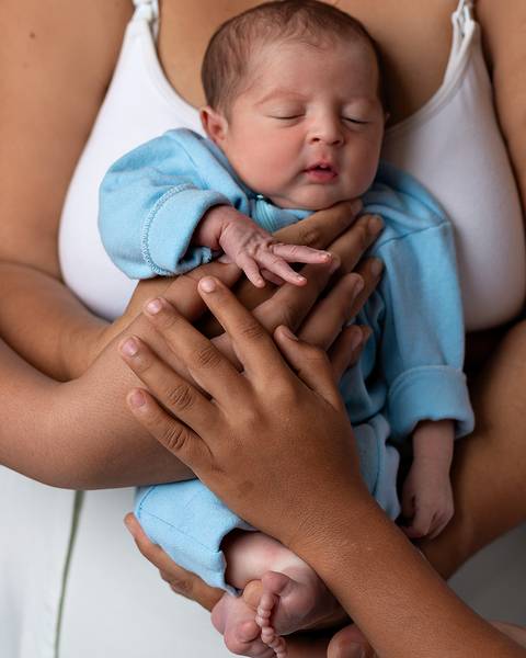 Ensaio Newborn Natal. Foto de recém-nascido com as mãos da família.'