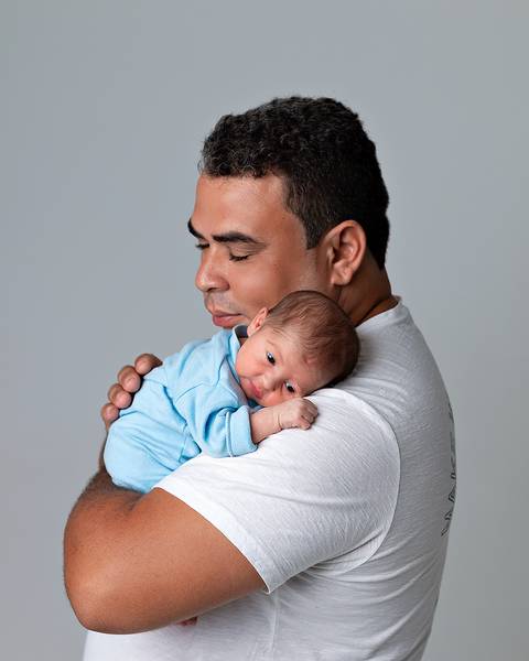 Ensaio de recém-nascido em Natal. Foto de bebê deitado no braço do pai.'