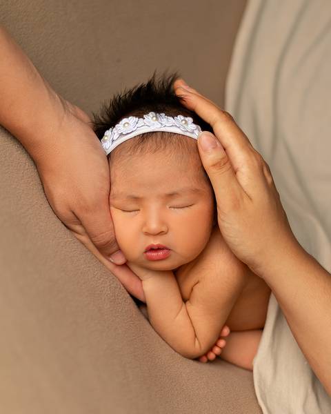 Close do rostinho do bebê com mãos dos pais ao redor. '