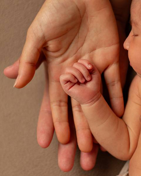 Close das mãos do bebê recém-nascido e pais em ensaio Newborn em estúdio.'
