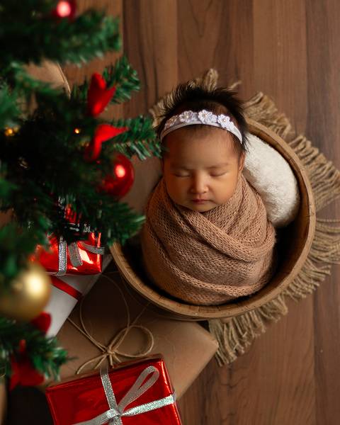 Bebê recém-nascida em fotos em estúdio com cenário natalino. bebê dentro de baldinho, enrolada no wrap.'