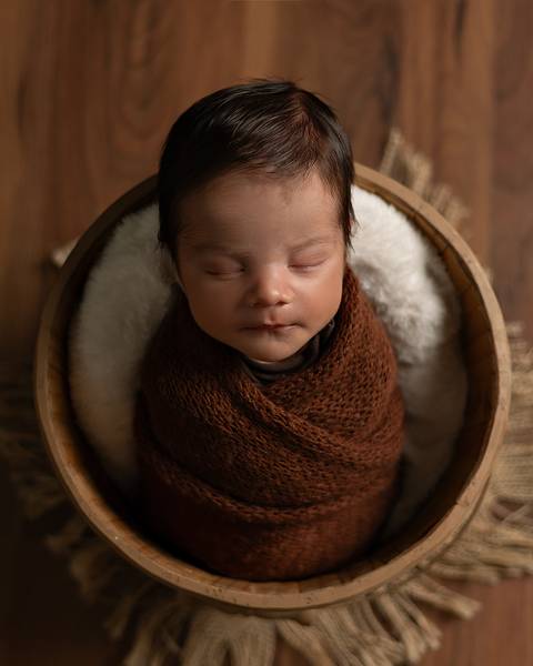 O bebê recém-nascido está dormindo enroladinho no wrap em seu ensaio de primeiros dias. '