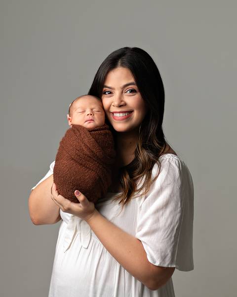 Ensaio Newborn em estúdio. Bebê recém-nascido enrolado no wrap nos braços da mãe. '