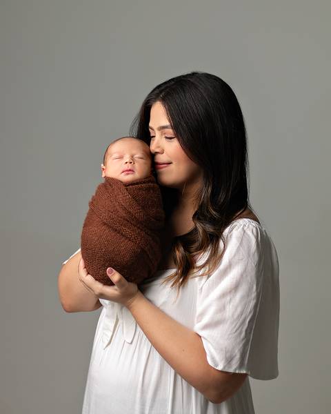 Ensaio Newborn em estúdio. Bebê recém-nascido enrolado no wrap nos braços da mãe. '