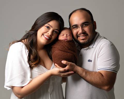 Ensaio Newborn em estúdio. Bebê recém-nascido enrolado no wrap nos braços dos pais.'