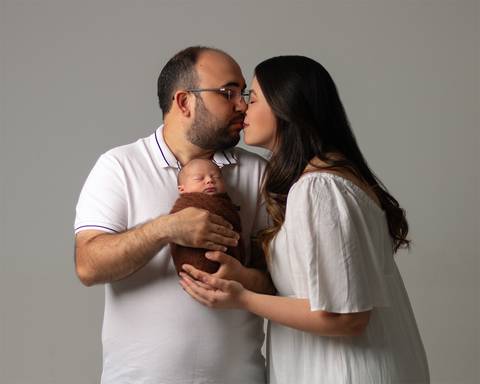 Ensaio Newborn em estúdio. Bebê recém-nascido enrolado no wrap nos braços dos pais.'