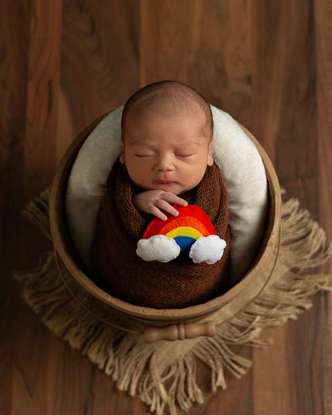 Ensaio Newborn em estúdio. Bebê recém-nascido dormindo em baldinho. Enrolado no wrap.'
