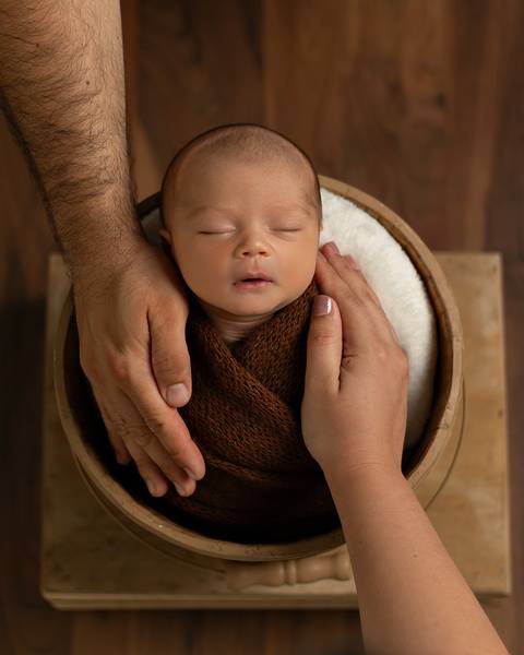 Ensaio Newborn em estúdio. Bebê recém-nascido dormindo em baldinho. Enrolado no wrap.'