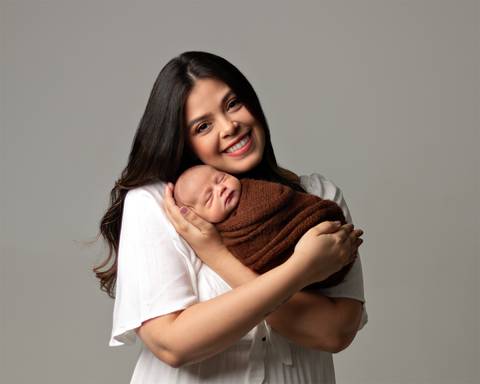 Ensaio Newborn em estúdio. Bebê recém-nascido enrolado no wrap nos braços da mãe. '