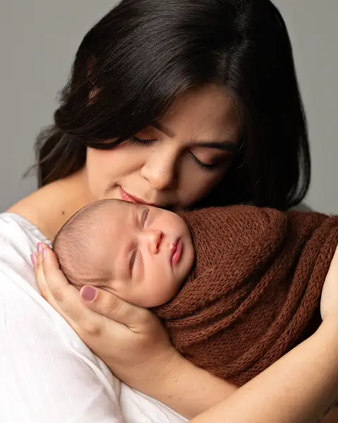 Ensaio Newborn em estúdio. Bebê recém-nascido enrolado no wrap nos braços da mãe. '