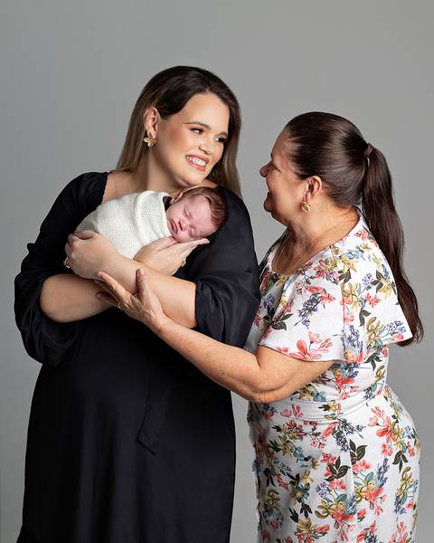Ensaio Newborn. Bebê enrolado no wrap sendo segurado pela mãe e a avó.'