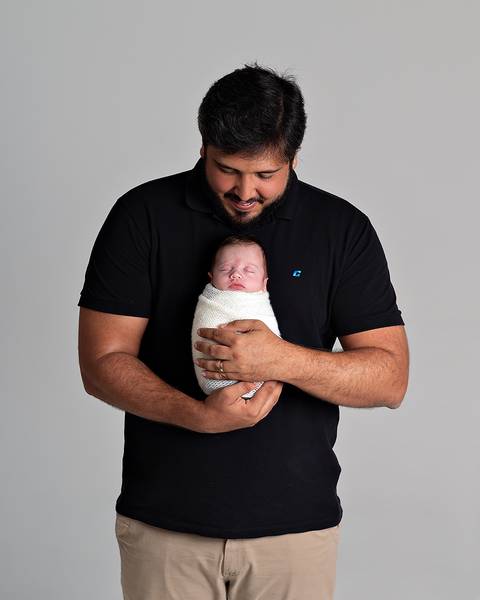 Ensaio Newborn. Bebê enrolado no wrap sendo segurado pelo pai.'