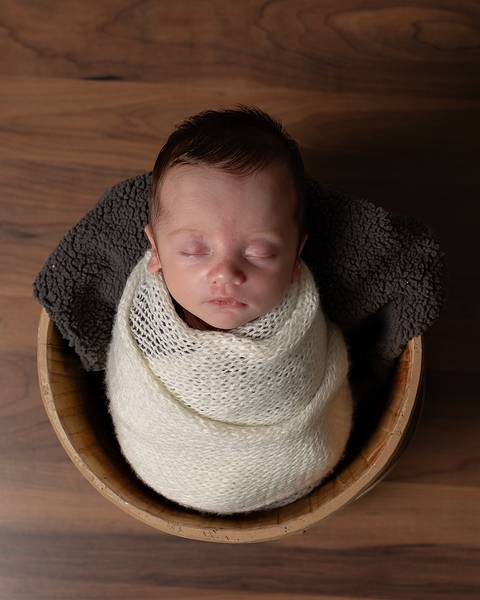 Bebê recém nascido enrolado no wrap dentro de baldinho. '