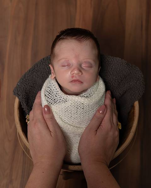 Bebê recém nascido enrolado no wrap dentro de baldinho. '