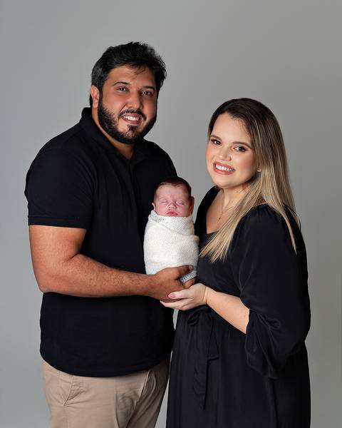 Ensaio Newborn. Bebê enrolado no wrap sendo segurado pelas mãos dos pais.'