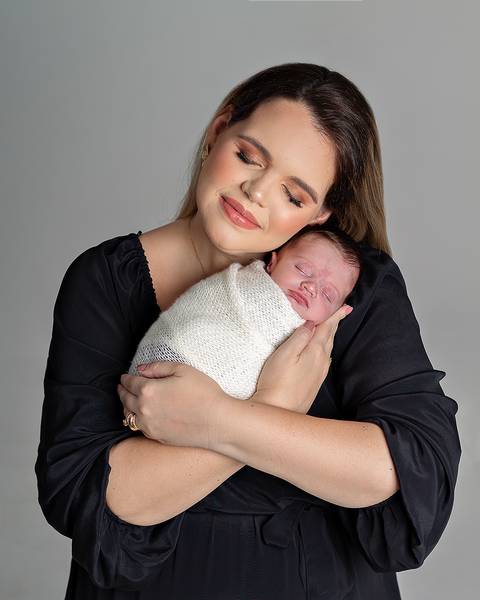 Ensaio Newborn. Bebê enrolado no wrap sendo segurado pela mãe.'