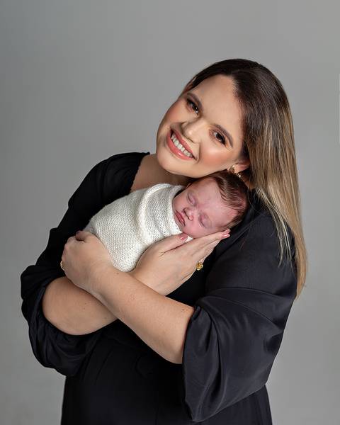 Ensaio Newborn. Bebê enrolado no wrap sendo segurado pela mãe.'