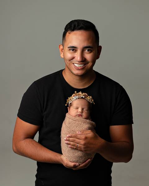 pai segurando filha recém-nascida enrolada no wrap em ensaio Newborn em estúdio.'