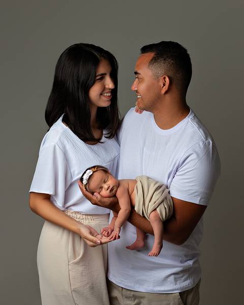 Bebê dormindo nos braços do pai, com a mãe ao lado, em ensaio Newborn em Natal/RN'