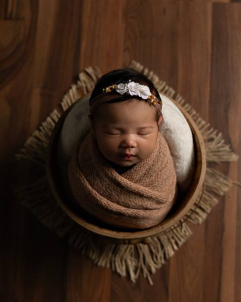 Bebê dormindo em ensaio newborn. Ela está entro de um baldinho e enrolada no Wrap.'