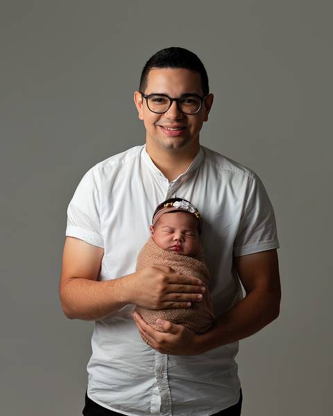 Bebê dormindo nos braços do pai em ensaio newborn'