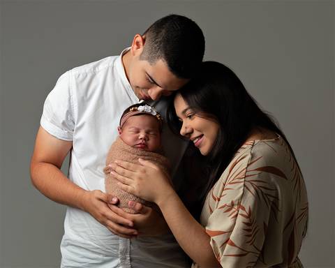 Bebê dormindo nos braços do pai e da mãe em ensaio newborn'