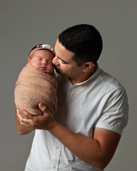 Bebê dormindo nos braços do pai em ensaio newborn'