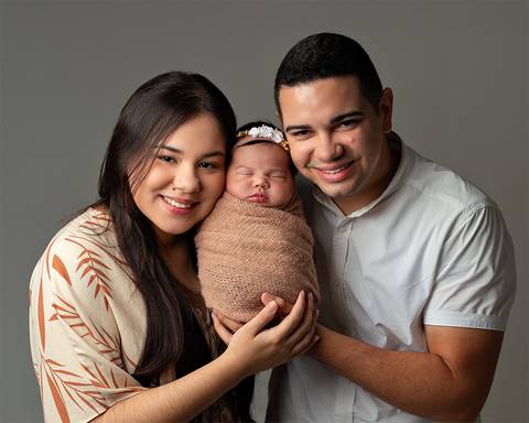 Bebê dormindo nos braços do pai e da mãe em ensaio newborn'