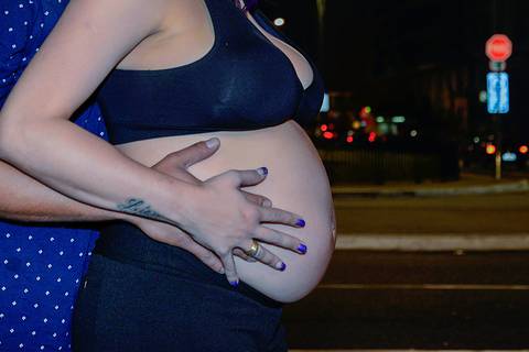mãos apoiadas na barriga da gestante em ensaio noturno na avenida paulista'
