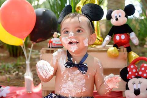 criança sorrindo suja de bolo no ensaio Smash the cake tema mickey no parque, decoraçao com as cores do tema, fotografa smash e infantil no tatuape e regiao'