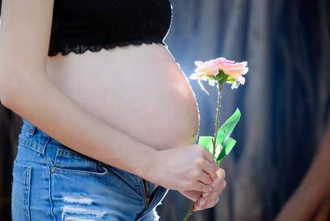 Gestante segurando flor na barriga, no parque, cenario com galhos,fotografa ensaio gestante externo, parque piqueri, tatuape.'