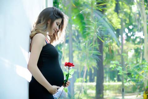 Gestante de roupa preta na natureza olhando para flor na barriga. fotografa ensaio gestante no tatuape, Fotos Gestante iluminaçao de cinema.'