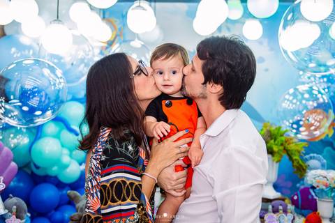 pais beijando criança em momento de carinho durante festa infantil tema fundo do mar'