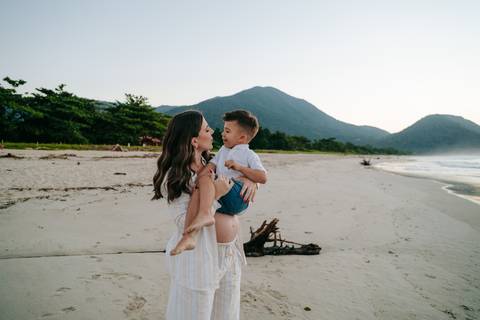 Gestante e seu filho compartilhando um momento de carinho durante ensaio fotográfico na praia.'