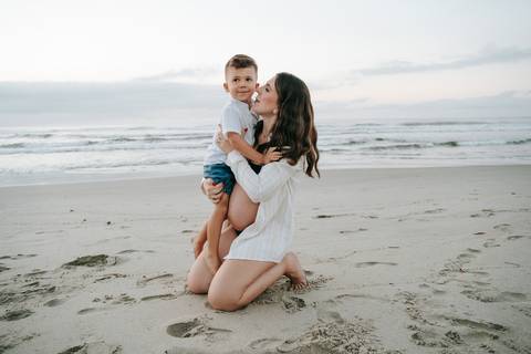 Gestante e seu filho compartilhando um momento de carinho durante ensaio fotográfico na praia.'