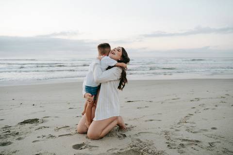 Gestante e seu filho compartilhando um momento de carinho durante ensaio fotográfico na praia.'