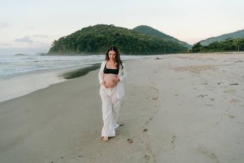Gestante caminhando na areia durante ensaio fotográfico na Praia de Itamambuca em Ubatuba.'