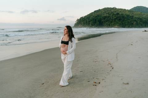 Gestante caminhando na areia durante ensaio fotográfico na Praia de Itamambuca em Ubatuba.'